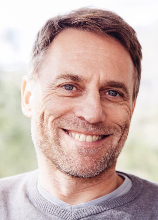 Middle-aged man smiling warmly at camera in professional headshot for dental practice.