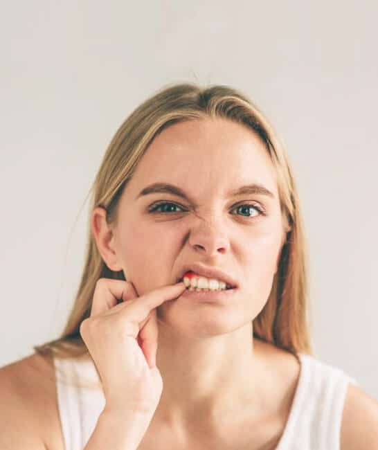 Woman biting fingernail with worried expression against white background