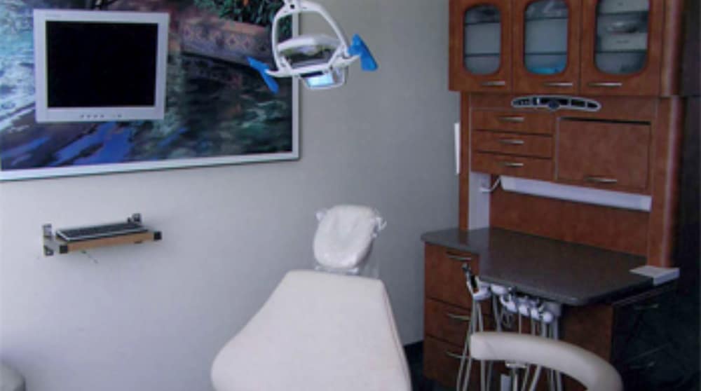 Modern dental treatment room in Poway with a patient chair, overhead light, wall-mounted monitor, and organized cabinetry for dental tools