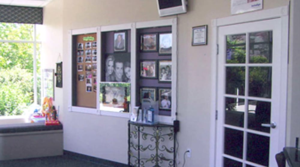 Bright and welcoming waiting area at a Poway dental office with family photo display, bulletin board, large window with natural light, and a white door leading to treatment rooms