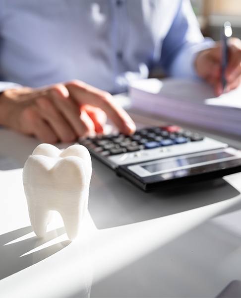 Dentist calculating costs at desk with tooth model and calculator visible.
