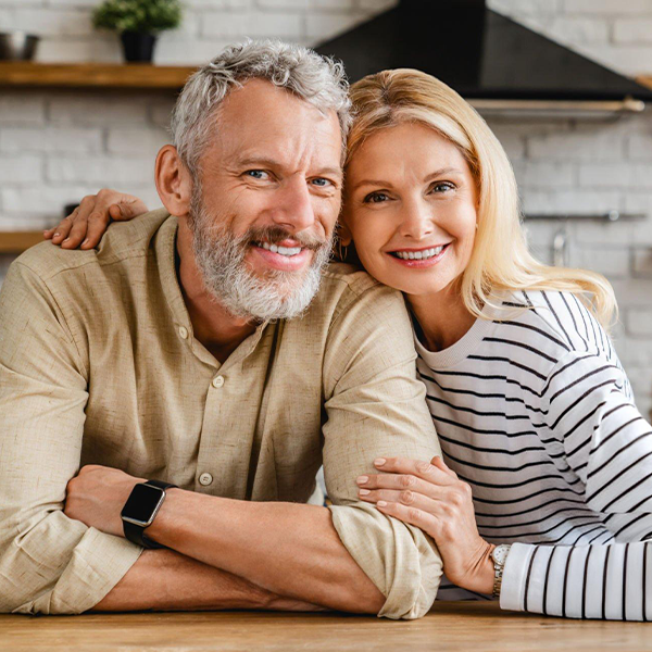 Smiling middle-aged couple posing together at wooden counter in modern home interior.