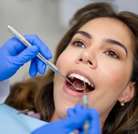 Woman receiving dental examination with dentist using tools and mirror in clinical setting.