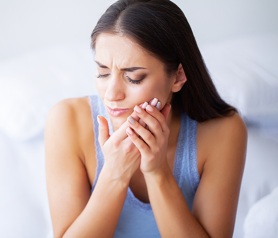 Woman with toothache holding jaw in pain, expressing dental discomfort indoors.