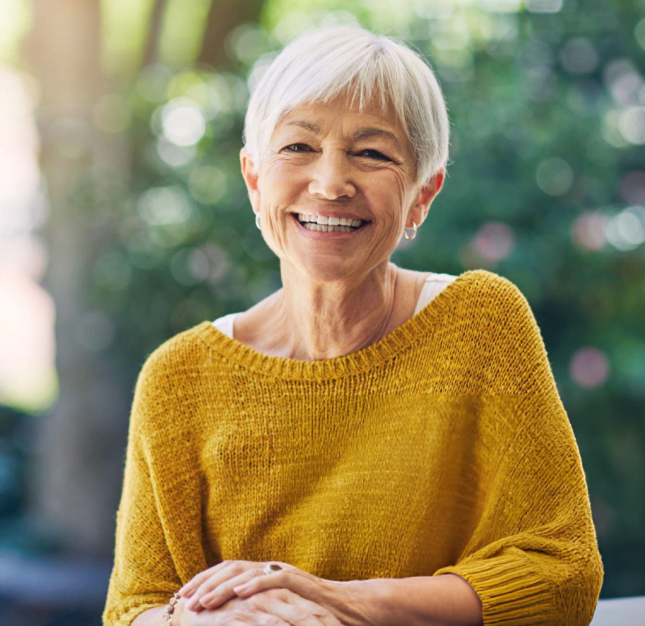 Smiling senior woman in yellow sweater outdoors with blurred green background.