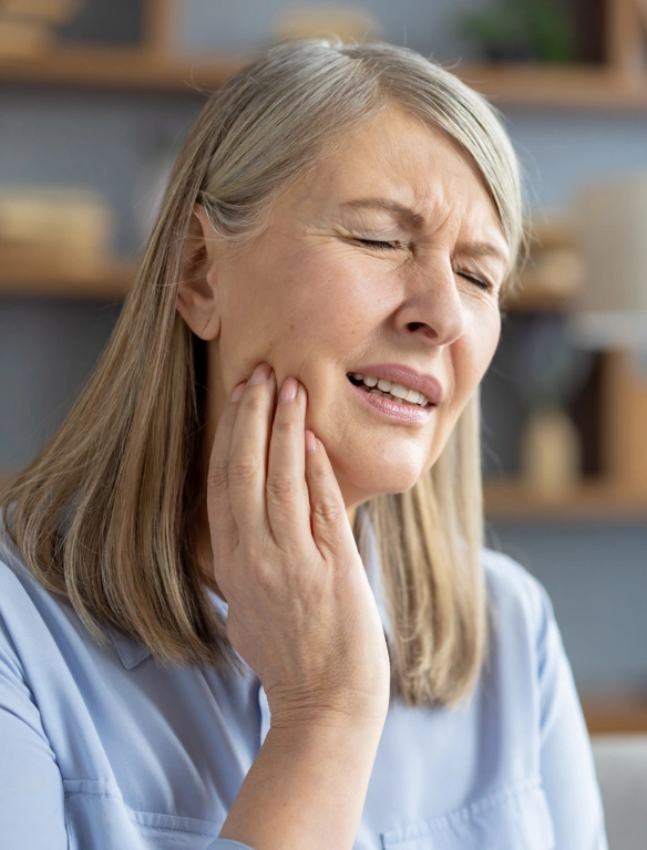 Woman experiencing tooth pain, holding jaw with hand, indoor medical setting.