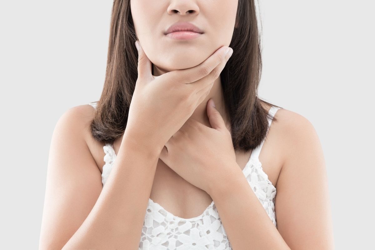 Woman touching her chin and neck area, appearing to experience jaw or dental discomfort, white background.